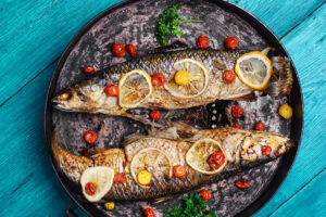 Frying pan with two baked fish in tomatoes,spices and lemon