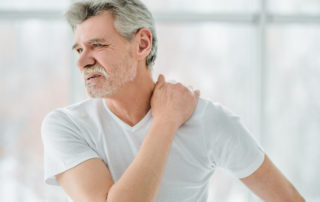 Senior man in white t-shirt holding his back in pain.